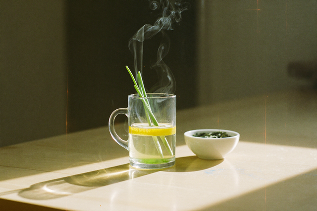 Glas mit frisch aufgegossenem grünem Tee und Zitrone im Morgenlicht