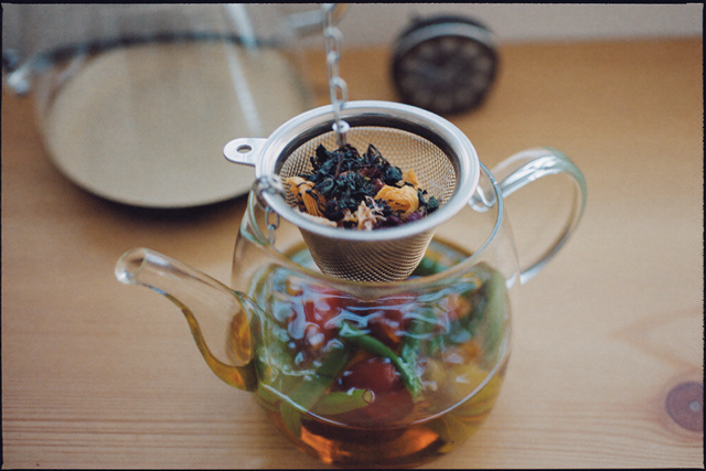 Teesieb mit losem Kräutertee in einer Glaskanne mit heißem Wasser